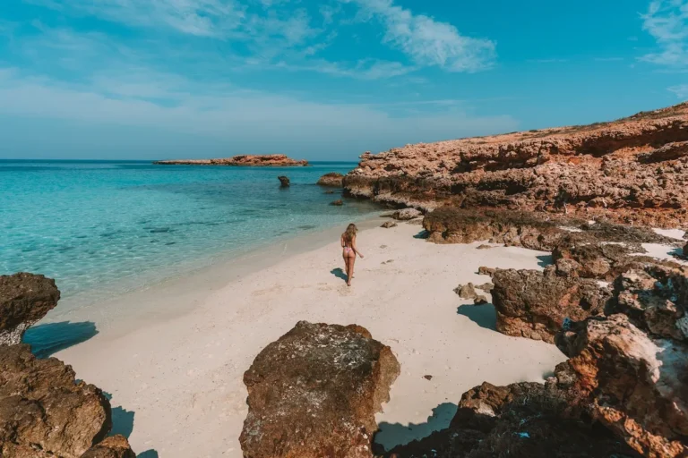 Guest walking on a white sand beach between red rocks on a Daymaniyat island