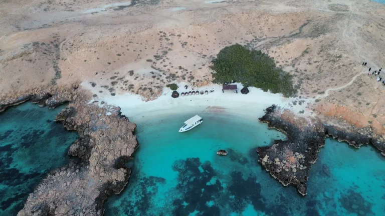 Aerial view of a turquoise bay with a tour boat at anchor and a small beach camp, Daymaniyat Islands