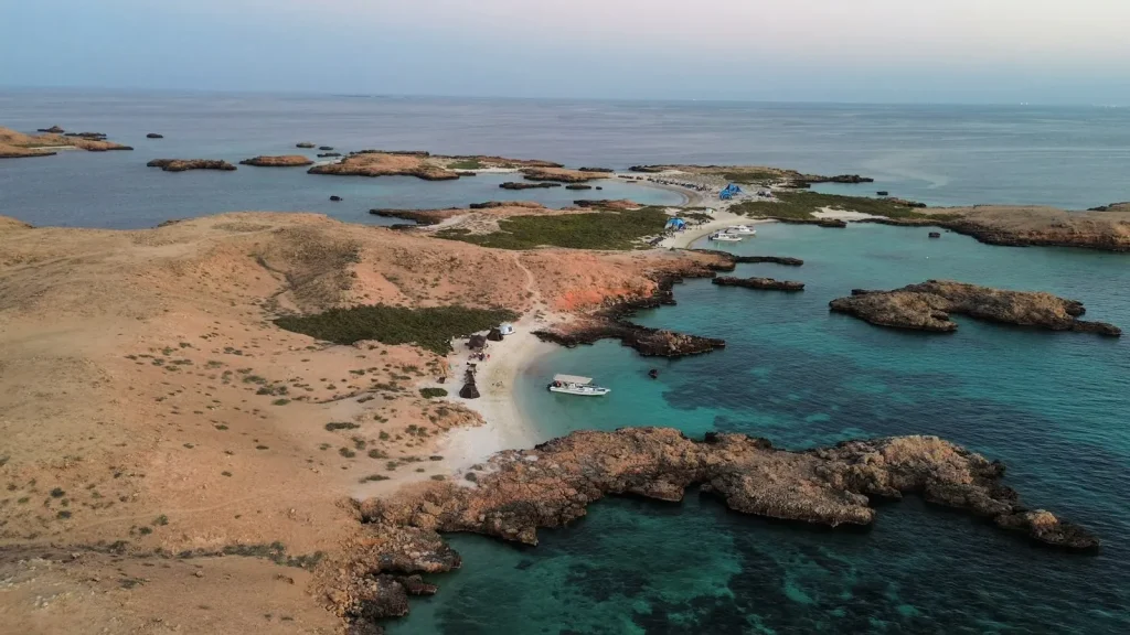 Wide aerial view of a Daymaniyat island and its turquoise lagoon at dusk, with a boat at anchor
