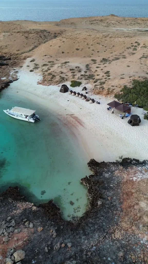 Aerial view at dusk of the island camp's tents on the beach with the boat anchored in the bay, Daymaniyat Islands