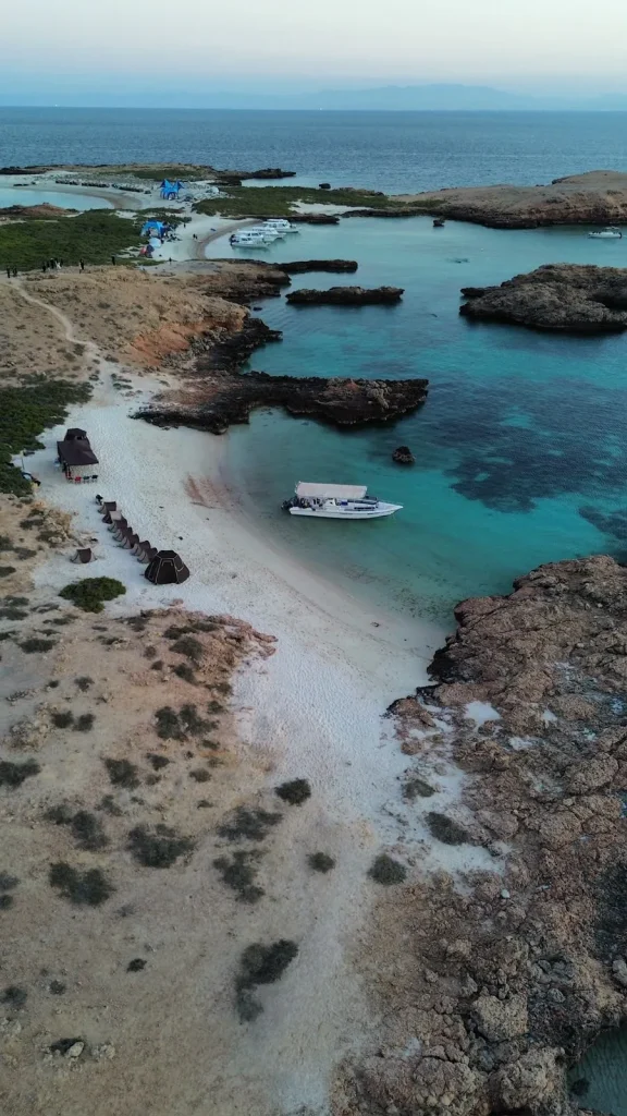 Aerial view over a sandy island lagoon with a boat at anchor and more islands stretching out to sea