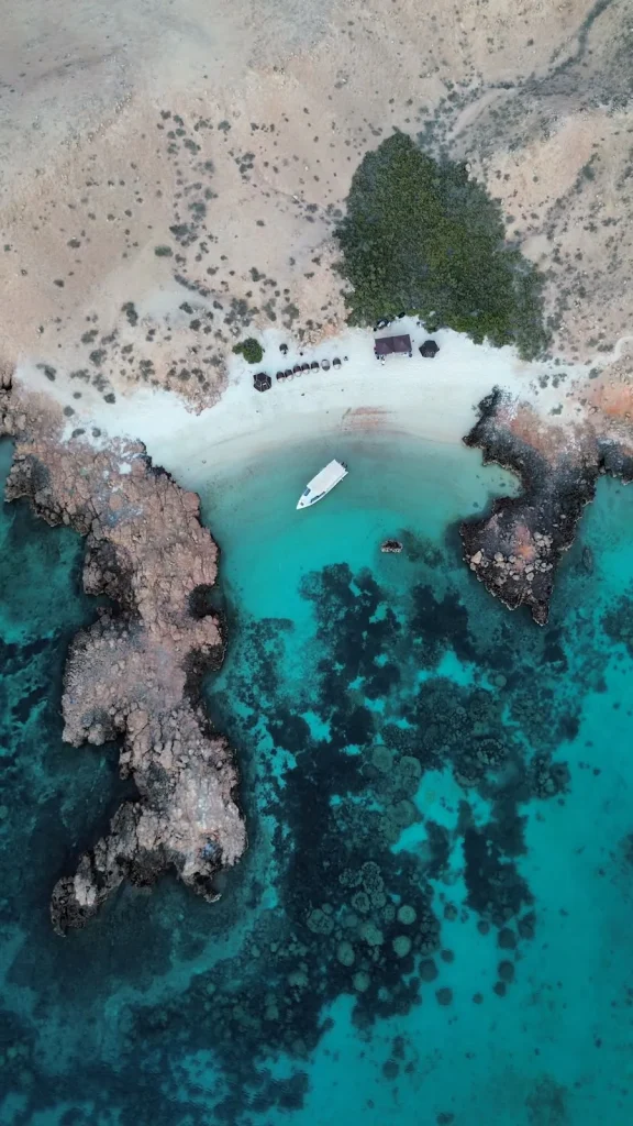Aerial view of a rocky bay with coral reef and a boat at anchor, Daymaniyat Islands