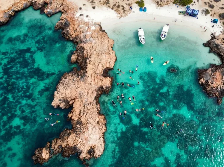 Aerial view of snorkelers at a coral reef with two boats anchored beside a white beach, Daymaniyat Islands