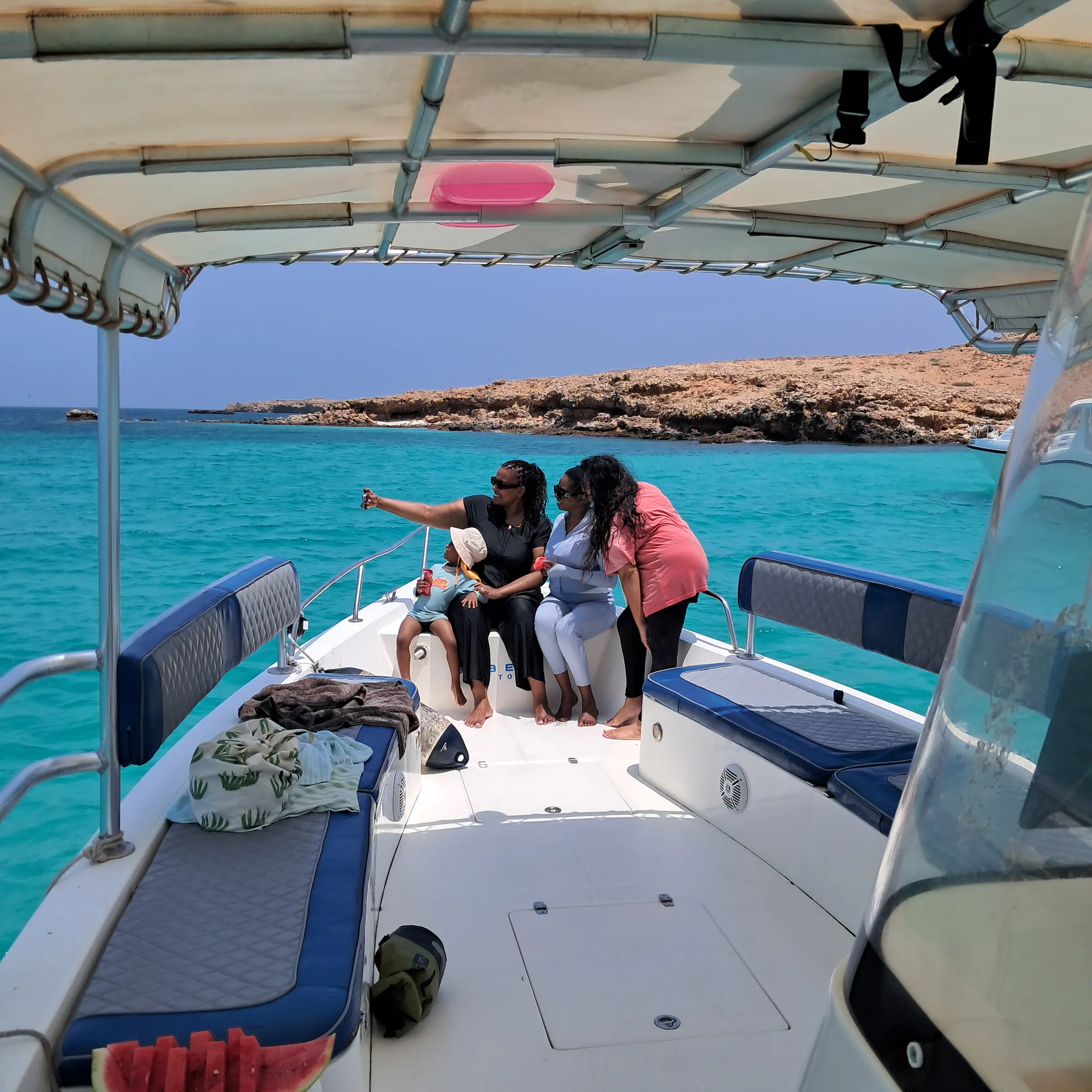 Wide view of the shaded boat deck with blue cushioned seats and guests, turquoise sea beyond