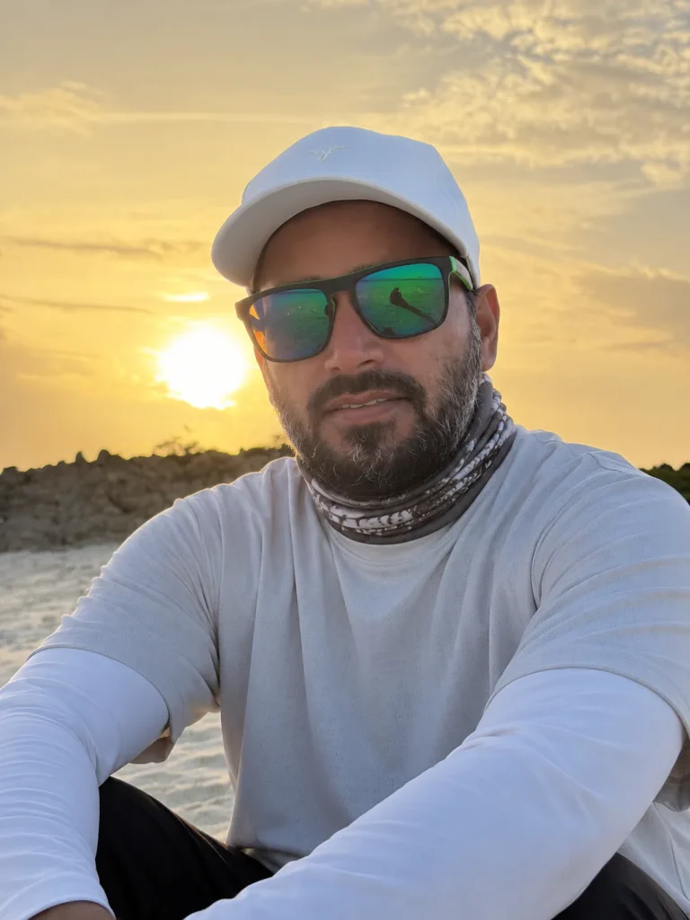 Captain Sufyan in a cap and sunglasses sitting on an island beach at sunset, Daymaniyat Islands