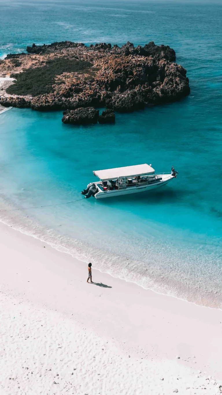 Boat floating in bright turquoise shallow water off a white sand beach, Daymaniyat Islands