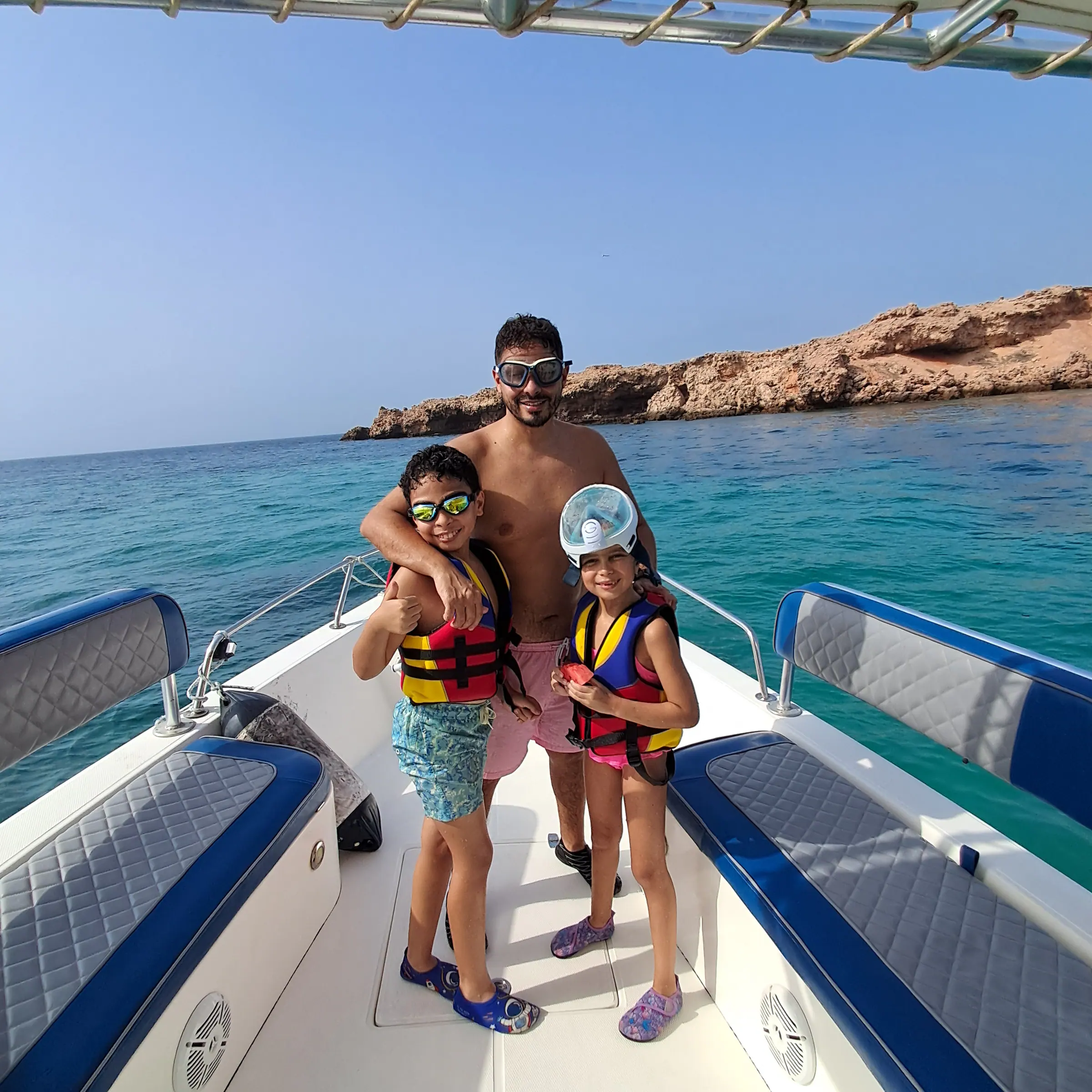 Family in life jackets and snorkel masks posing at the front of the boat with the sea behind