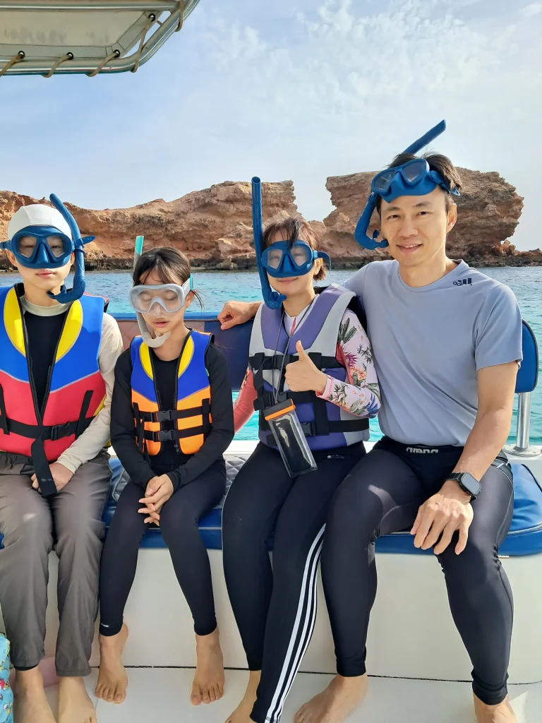 Family in life jackets and snorkel masks sitting on the boat before snorkeling at the Daymaniyat Islands