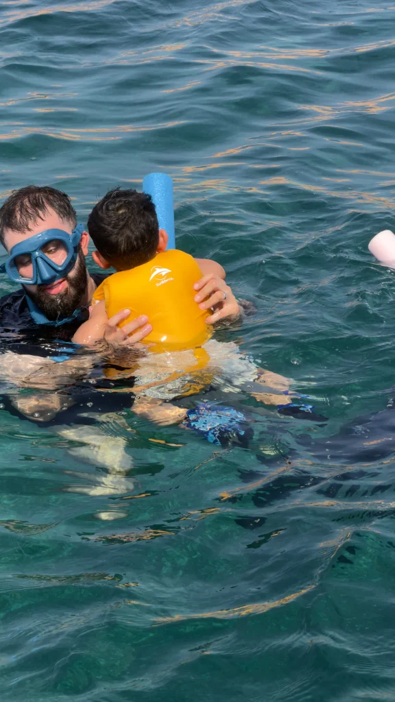 Father snorkeling in the open sea with his young child wearing a life jacket