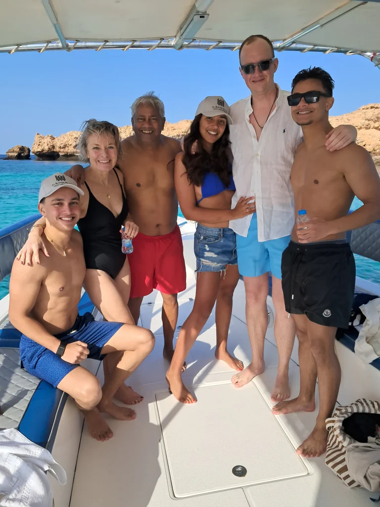 Group of six smiling guests posing together on the deck of a snorkeling boat near the Daymaniyat Islands