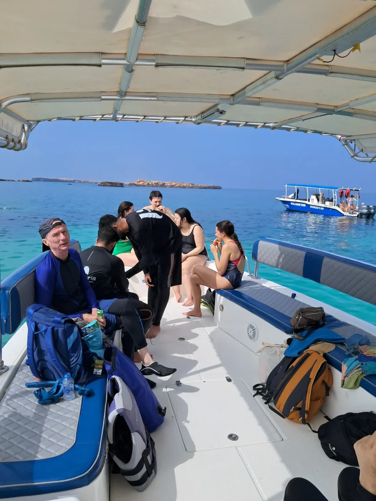 Guests getting ready on the boat deck with snorkeling gear and bags, another tour boat in the distance