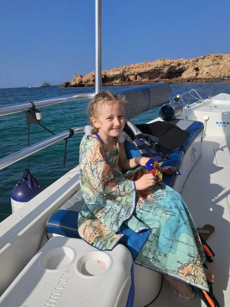 Young guest sitting on a blue boat seat with a rocky island in the background